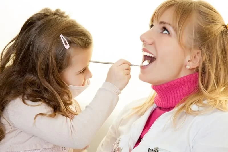 A little girl playing dentist and examining the doctor's teeth
